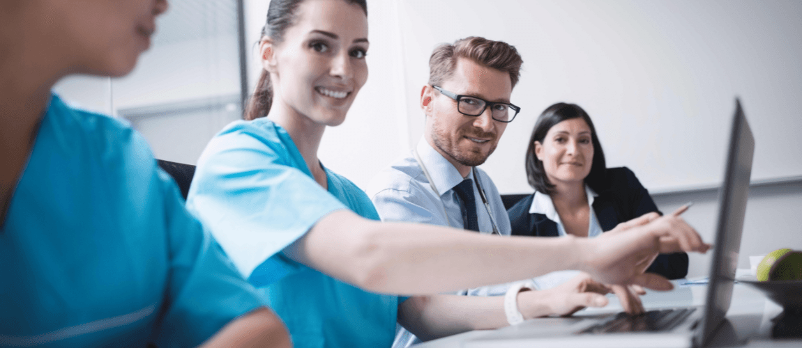 Mehrere Menschen sitzen in Berufskleidung an einem Tisch und blicken in die Kamera.