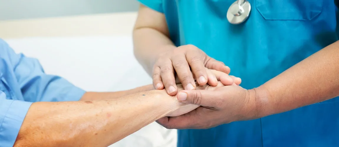 Eine Pflegefachkraft hält die Hände einer anderen Person in den Händen.