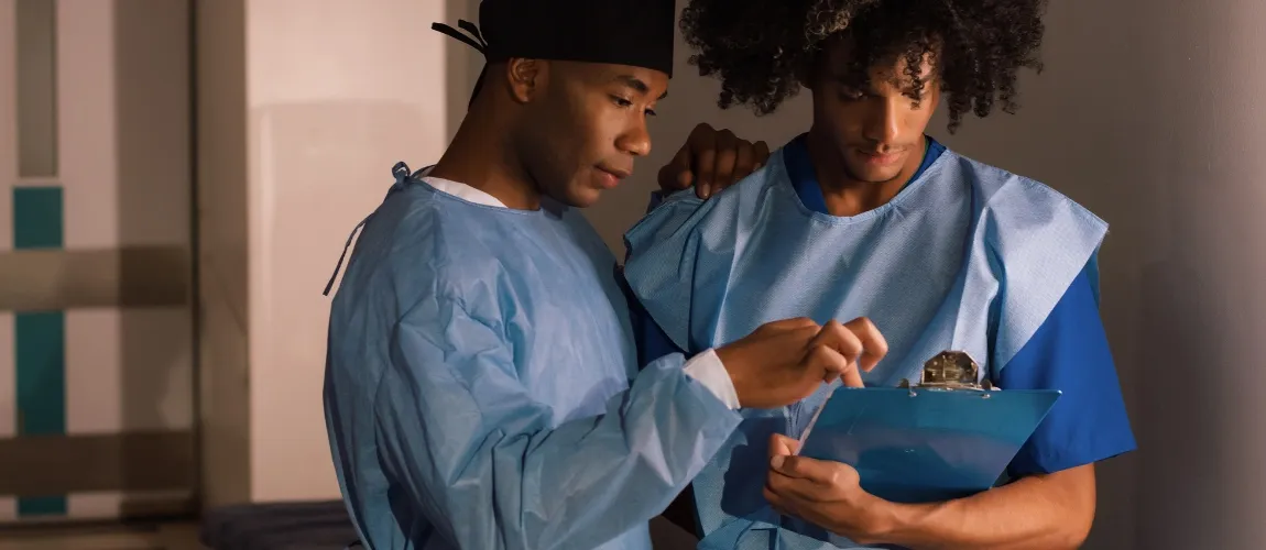 Eine Pflegefachkraft deutet mit dem Finger auf ein Klemmbrett, das eine Person in der Hand hält.