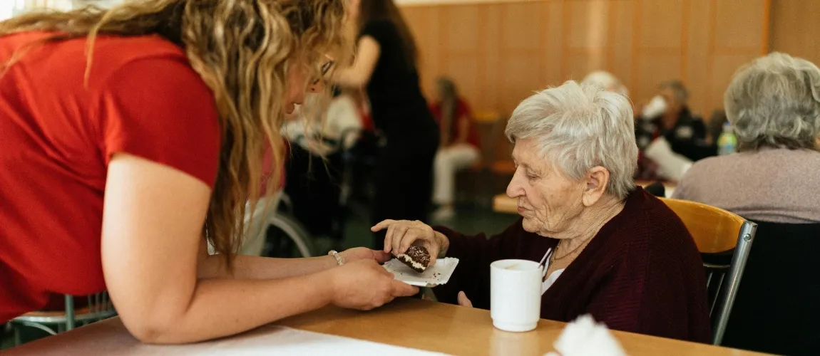 Eine Seniorin nimmt ein Stück Gebäck, das ihr gereicht wird.