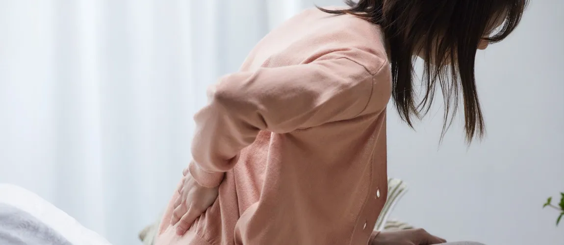 Eine Frau sitzt im Bett und hält sich vor Schmerzen den Rücken.