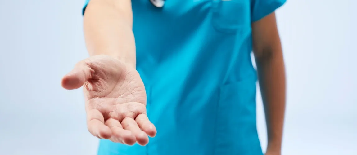 Ein Mensch mit Pflegekleidung streckt die Hand in Richtung Kamera aus.