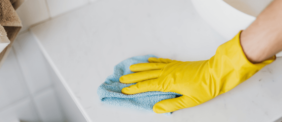 Eine Person mit gelben Gummihandschuhen wischt eine Fläche mit einem Lappen ab.