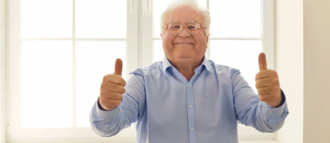 Ein Senior hält beide Daumen nach oben und lächelt.