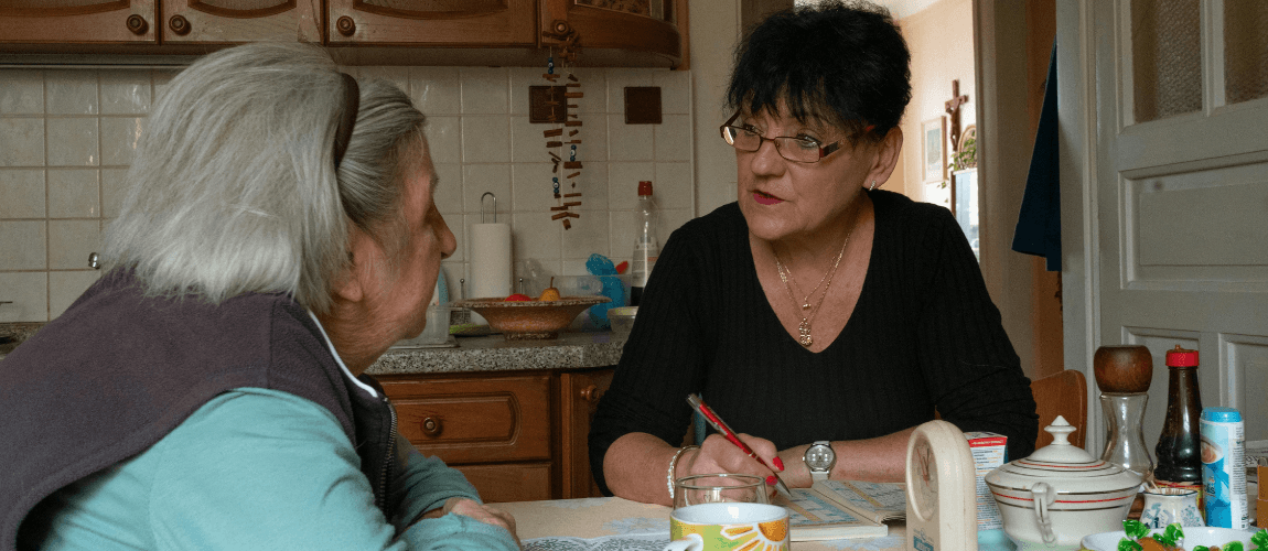 Eine Frau sitzt einer Seniorin in der Küche gegenüber.